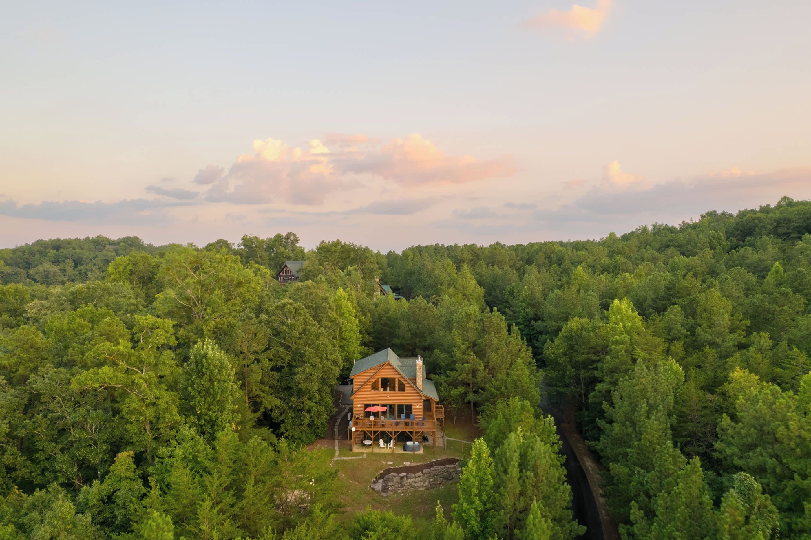 A wooden cabin surrounded by dense forest, with a clear sky above.