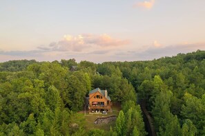 A wooden cabin surrounded by dense forest, with a clear sky above.