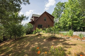 A two-story log cabin with a sloped roof, surrounded by a well-maintained garden and trees. - Mountain View Cabin|Hot Tub|Fenced Yard for Pets (Mill Spring)