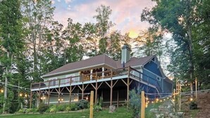 Une maison à deux étages avec une terrasse, entourée d’une pelouse et d’arbres.