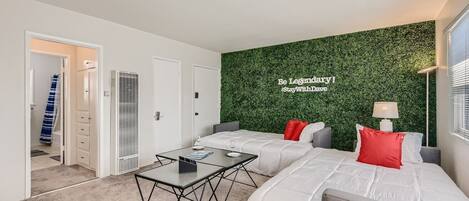 A modern hotel room with two beds, a small table, and a green wall with a motivational quote.