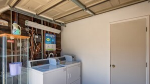 Uma lavanderia com máquina de lavar, secadora e um box de vidro com uma embalagem de detergente.