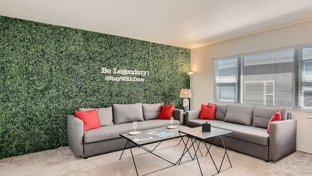 Uma sala de estar moderna com parede verde, sofás cinzas e almofadas vermelhas, e uma mesa de centro.