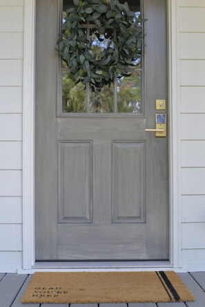 Una puerta delantera gris con un felpudo, una ventana pequeña y un timbre.
