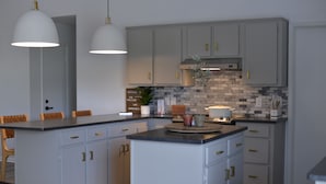 Una cocina moderna con armarios grises, una isla central, iluminación colgante y un salpicadero con una mezcla de baldosas blancas y grises.