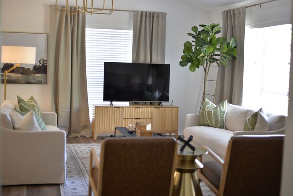 Ein modernes Wohnzimmer mit einem Flachbildfernseher, zwei Sofas, einem Couchtisch und einer großen Pflanze.