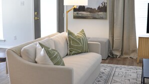 Una sala de estar con un sofá, una lámpara de pie, un cuadro en la pared y una ventana con cortinas.