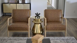 Una sala de estar moderna con dos sillones de cuero marrón, una mesa de latón con un centro decorativo geométrico negro y una alfombra estampada.