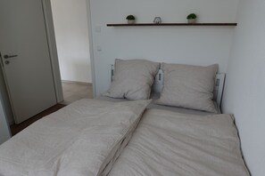 Un dormitorio con dos camas individuales, una puerta y una estantería con dos plantas en macetas.
