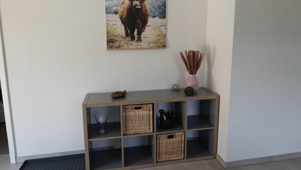 Ein Flur mit einem Holzkonsolentisch, Korbwäsche, einer Vase und einem Bilderrahmen mit einem Yak-Bild.