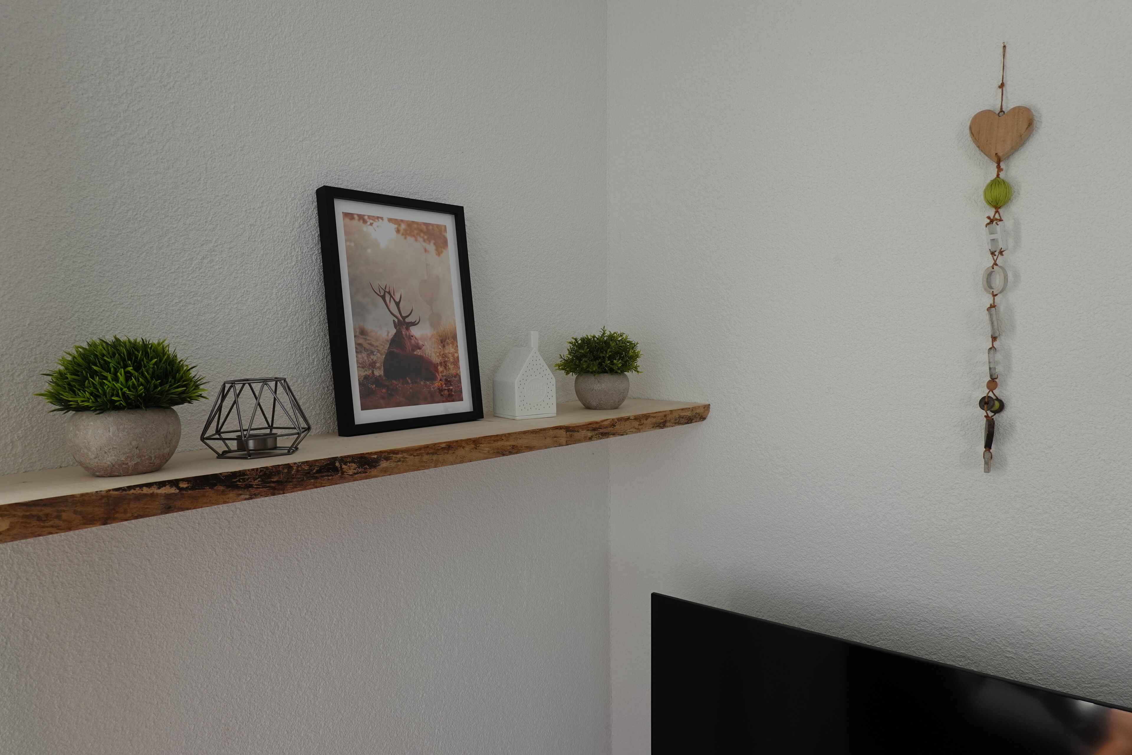 A wooden shelf with a framed picture, two potted plants, and a wall hanging.