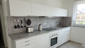 Eine moderne Küche mit weißen Schränken, einer Edelstahl-Dunstesse, einem Einbauofen und einem Fenster mit Jalousien.