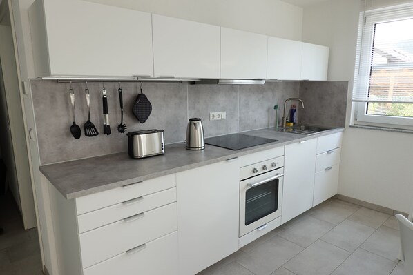 Una cocina moderna con gabinetes blancos, una campana extractora de acero inoxidable, un horno empotrado y un ventanal con persianas.