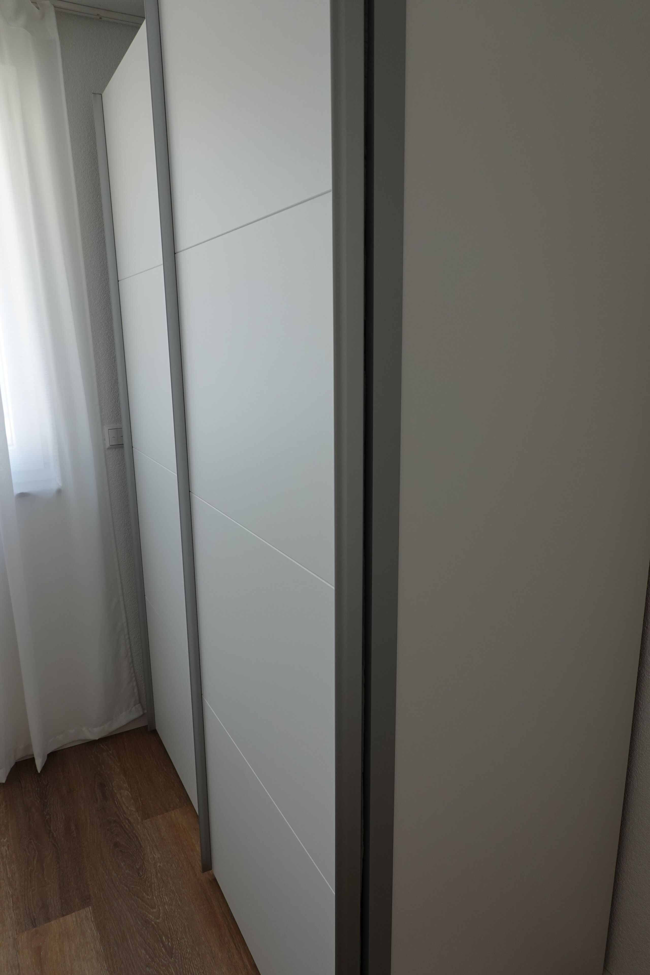 Ein schmaler Korridor mit Holzboden, einer weißen Tür und einer hellen Wand.