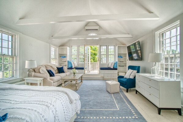 A spacious bedroom with a large bed, a sofa, a chair, a dresser, and a TV.