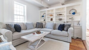 Een moderne woonkamer met een lichtgrijze modulaire bank, een witte salontafel en een ingebouwde witte kastenwand met decoratieve objecten.
