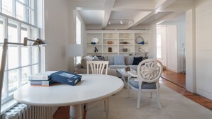 Een lichte, goed verlichte kamer met een witte tafel, stoelen en een boekenplank vol boeken en decoratieve voorwerpen.