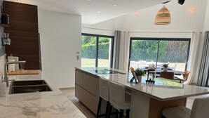 A modern kitchen with a large island, bar stools, and a view of the outdoors.