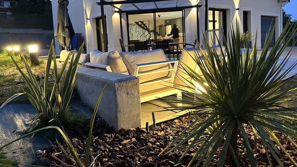 A modern house with a patio area featuring a sofa, a dining table, and a pergola.