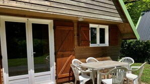 Una terraza de madera con una mesa, sillas, un ventanal corredero y un ventanuilla.
