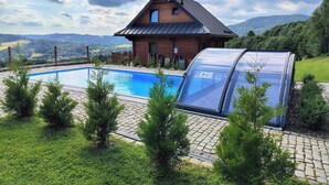 A house with a swimming pool, a covered outdoor area, and a view of the surrounding landscape.
