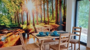 A dining area with a table set for four, wooden chairs, and a forest mural on the wall.