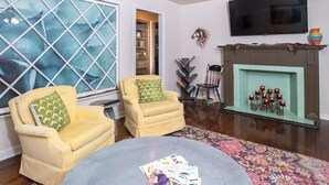 A living room with two yellow armchairs, a round coffee table with magazines, a fireplace with red candles, and a large window with a geometric pattern. - Horsefeathers 🐾 pet friendly funky comfort (Amarillo)