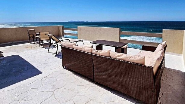 Un patio con mobiliario de mimbre, una mesa y vista al océano.