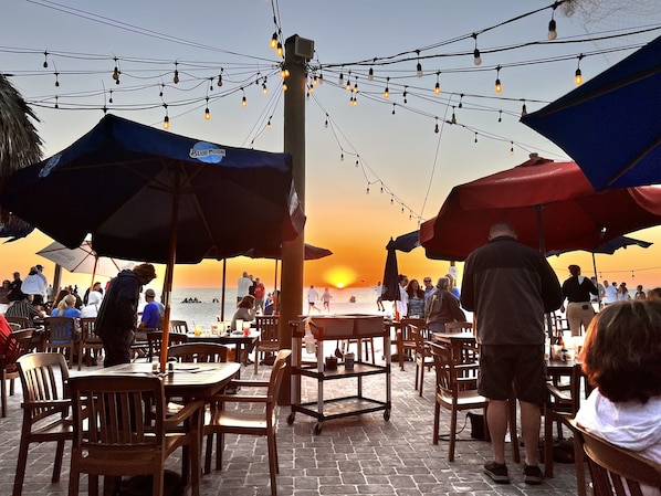 Un espace extérieur aménagé avec des tables, des chaises, des parasols et des guirlandes lumineuses.
