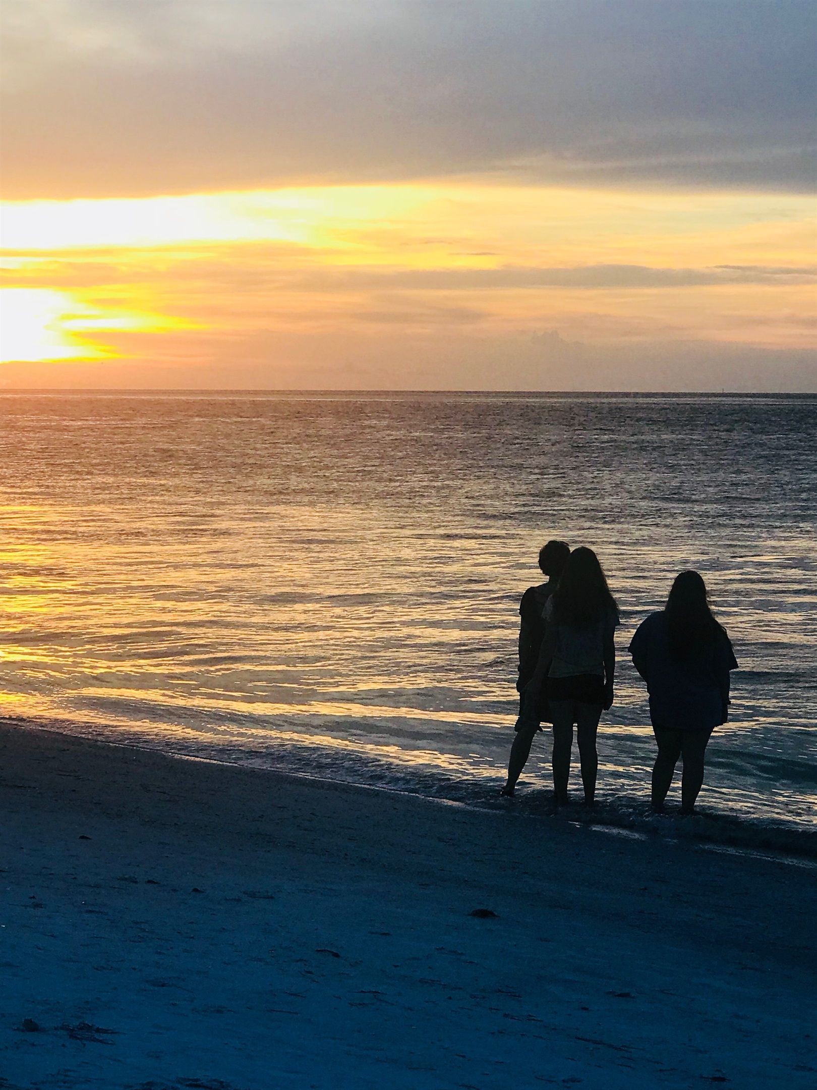 A sunset over a beach with three people silhouetted against the sky.