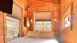 A wooden cabin bedroom with a bed, windows, and a guitar. - Dreamy Treehouse Getaway ~Dog Friendly~Disc Golf (Copperhill)