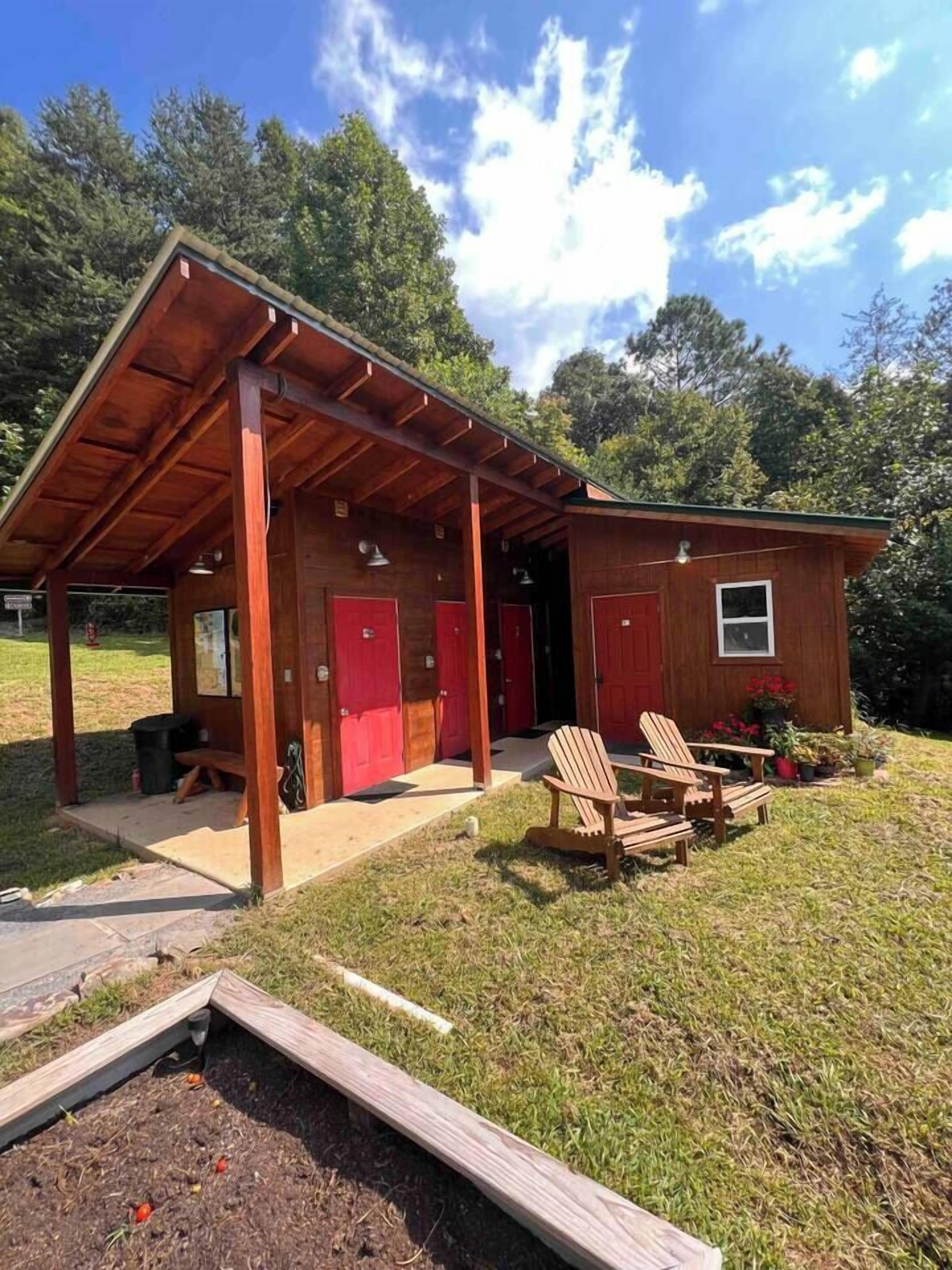A wooden cabin with a covered porch, red doors, and a small garden area with outdoor seating.