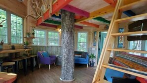 Un intérieur en bois avec un tronc d’arbre central, des poutres colorées et un escalier en bois.