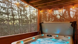 A hot tub with a wooden exterior, a window with a view of trees, and a ceiling with hanging lights.