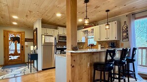 A kitchen with wooden cabinets, a stainless steel refrigerator, a microwave, and a bar area with stools.