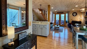 A spacious living area with wooden floors, a large mirror, a dining table, and a kitchen area with cabinets and a countertop.