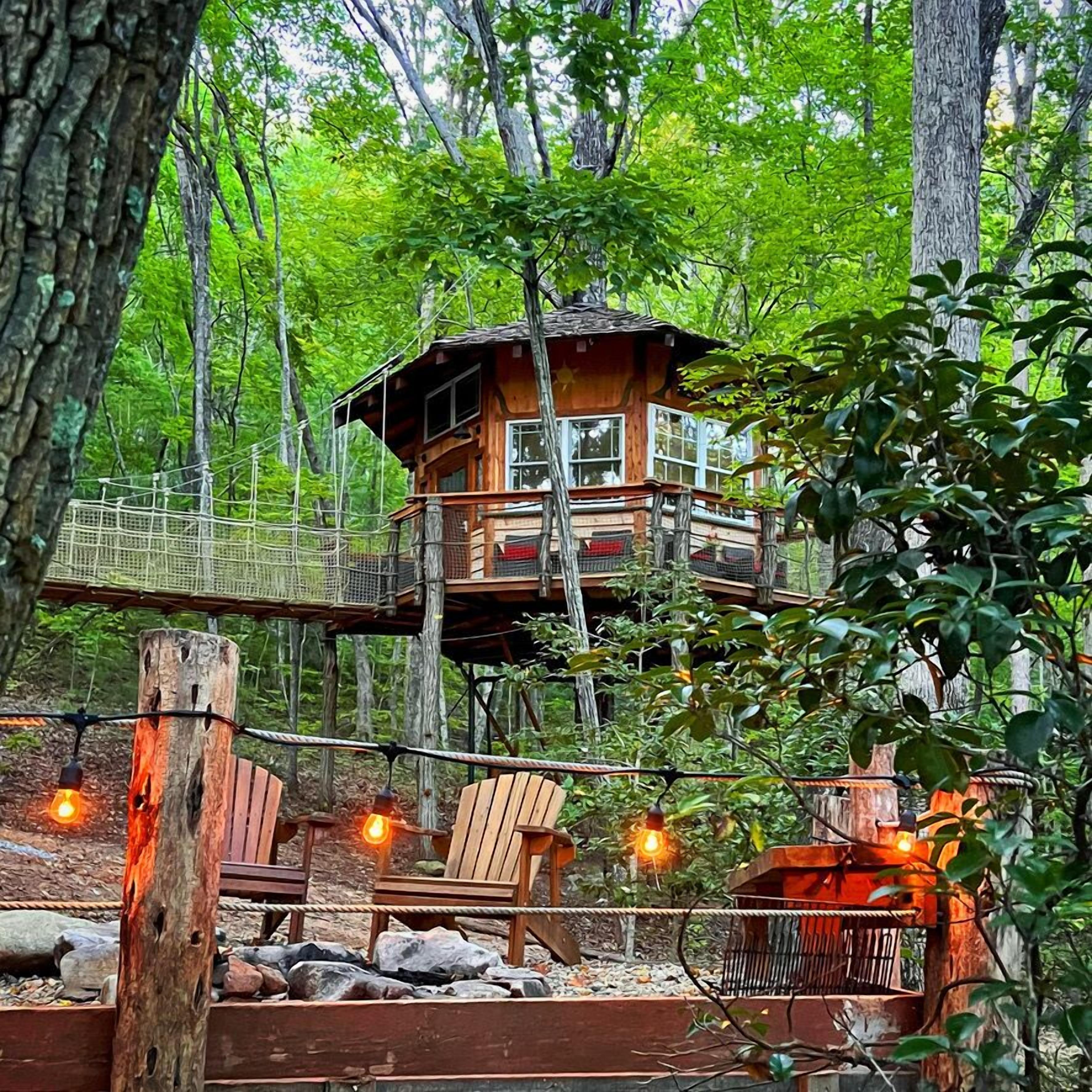 Una casa en el árbol con terraza de madera y un puente colgante.