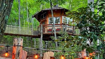 Una casa en el árbol con terraza de madera y un puente colgante.