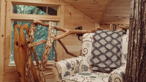 Un interno accogliente di una baita con soffitto in legno, una poltrona imbottita con cuscino decorato e una scala rustica.
