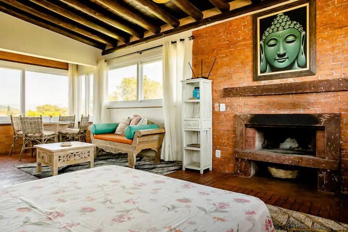 A cozy room with a bed, a sofa, a fireplace, and a Buddha statue.