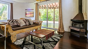 Una sala de estar con sofá, mesa de centro, chimenea y vistas a la vegetación a través de amplios ventanales.