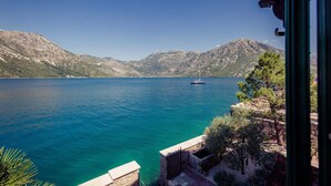 Vista di un lago calmo con una barca a vela, circondato da colline rocciose e vegetazione.