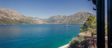 Vista de un lago tranquilo con un velero, rodeado de colinas rocosas y vegetación.