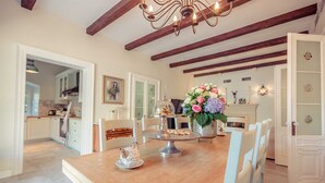 Zona pranzo con tavolo in legno, sedie, un lampadario e un vaso di fiori.