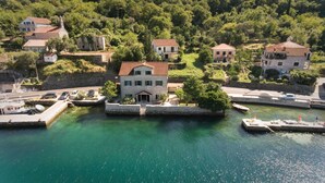 Una proprietà costiera con un edificio centrale circondato dall'acqua, collegata a un porto turistico con barche.