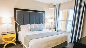 Une chambre d’hôtel avec un grand lit, deux tables de chevet, une petite table et une fenêtre avec des rideaux.