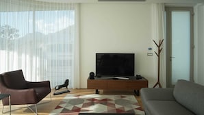 A modern living room with a large flat-screen TV, a brown leather sofa, a grey sofa, and a patterned rug. - Dukley Penthouse 3 Bedrooms (Budva)