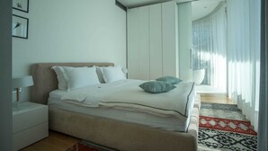 A modern bedroom with a bed, nightstands, a wardrobe, and a view of a balcony. - Dukley Penthouse 3 Bedrooms (Budva)