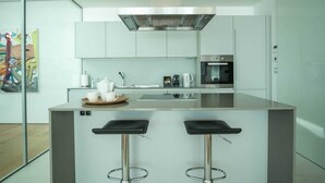 A modern kitchen with a central island, stainless steel appliances, and two bar stools. - Dukley Penthouse 3 Bedrooms (Budva)