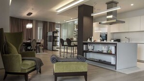 A modern living room with a green armchair, a small sofa, and a dining area with a glass table and chairs. - Dukley Penthouse 3 Bedrooms (Budva)